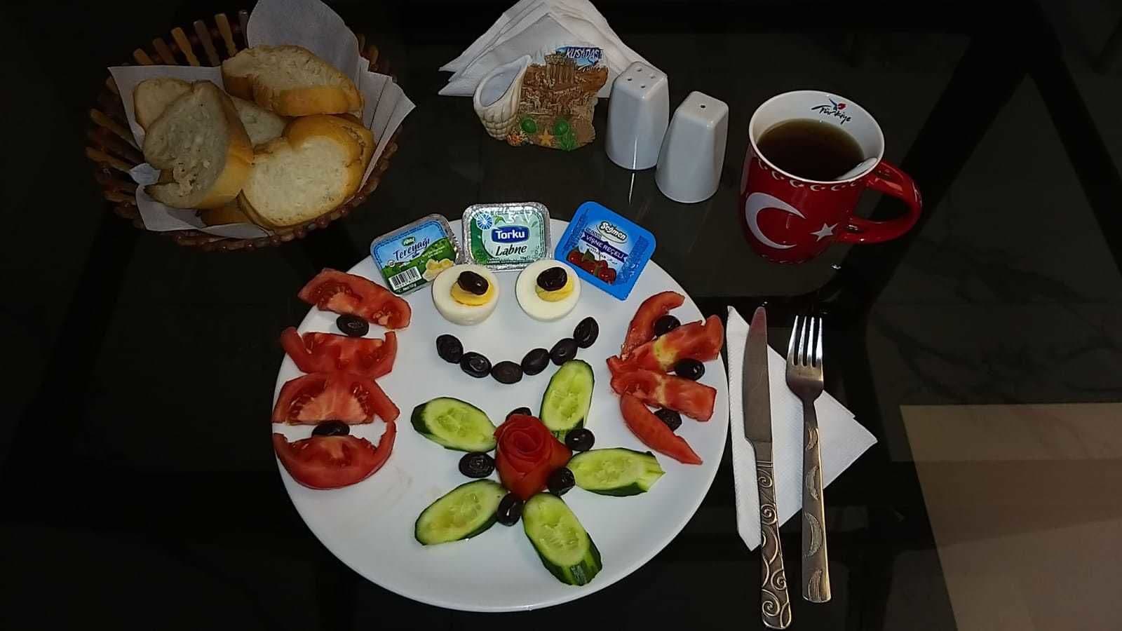 A breakfast table with bread, eggs, tomatoes, cucumbers, olives, and condiments.