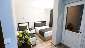 A bedroom with two beds, a nightstand, a vase with flowers, and a door with a window. - Papillonada Hotel (Kusadasi)