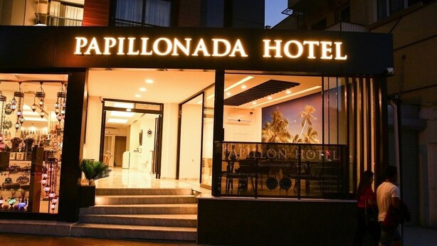 The Papillonada Hotel entrance with a well-lit facade, a visible staircase leading to the entrance, and a large poster advertising the hotel. - Papillonada Hotel (Kusadasi)