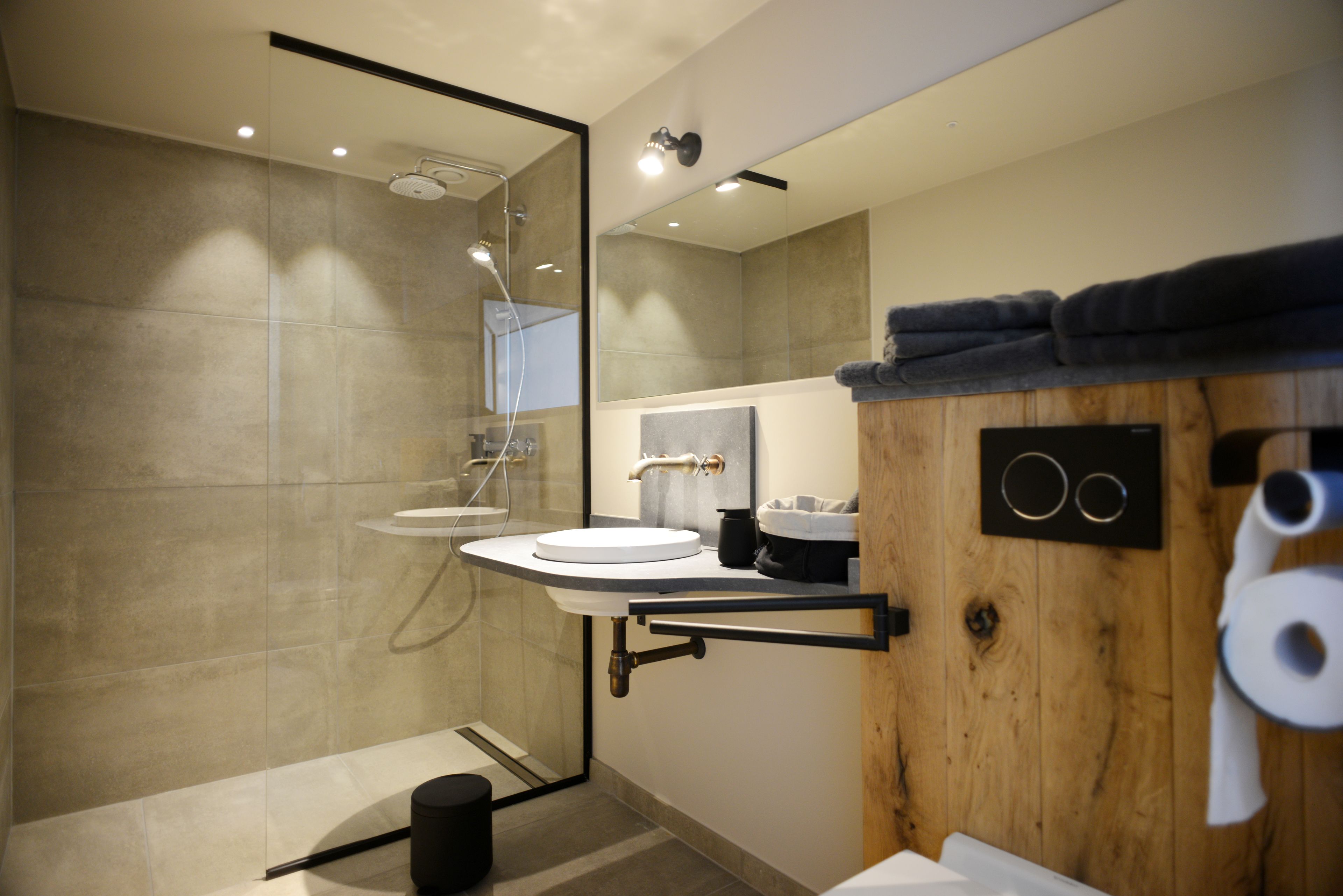 Un baño moderno con cabina de ducha de vidrio, lavabo con mueble de madera y toallero.