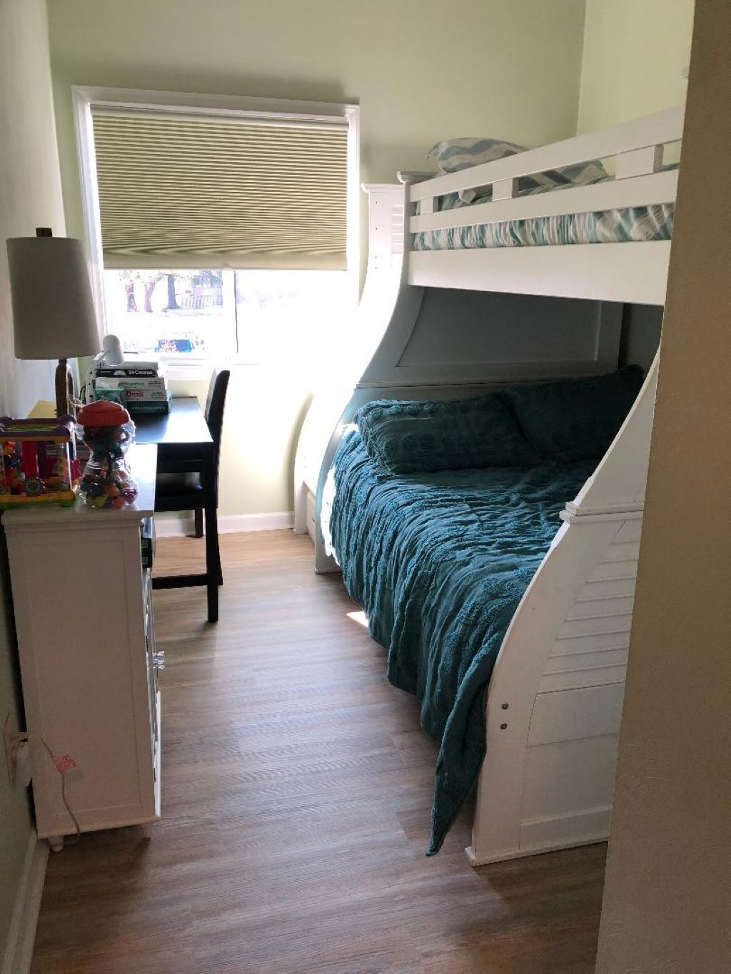 A compact room with a bunk bed, a desk with a chair, and a window with blinds.