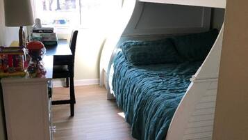 A compact room with a bunk bed, a desk with a chair, and a window with blinds.