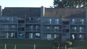 A multi-story residential building with balconies, a grassy area, and a dock extending into a body of water. - Fall is a great time for a relaxing getaway at Birds Eye View, Bernard's Landing (Moneta)