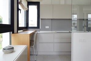 A modern kitchen with white cabinetry, a wooden countertop, and a window with a curtain.