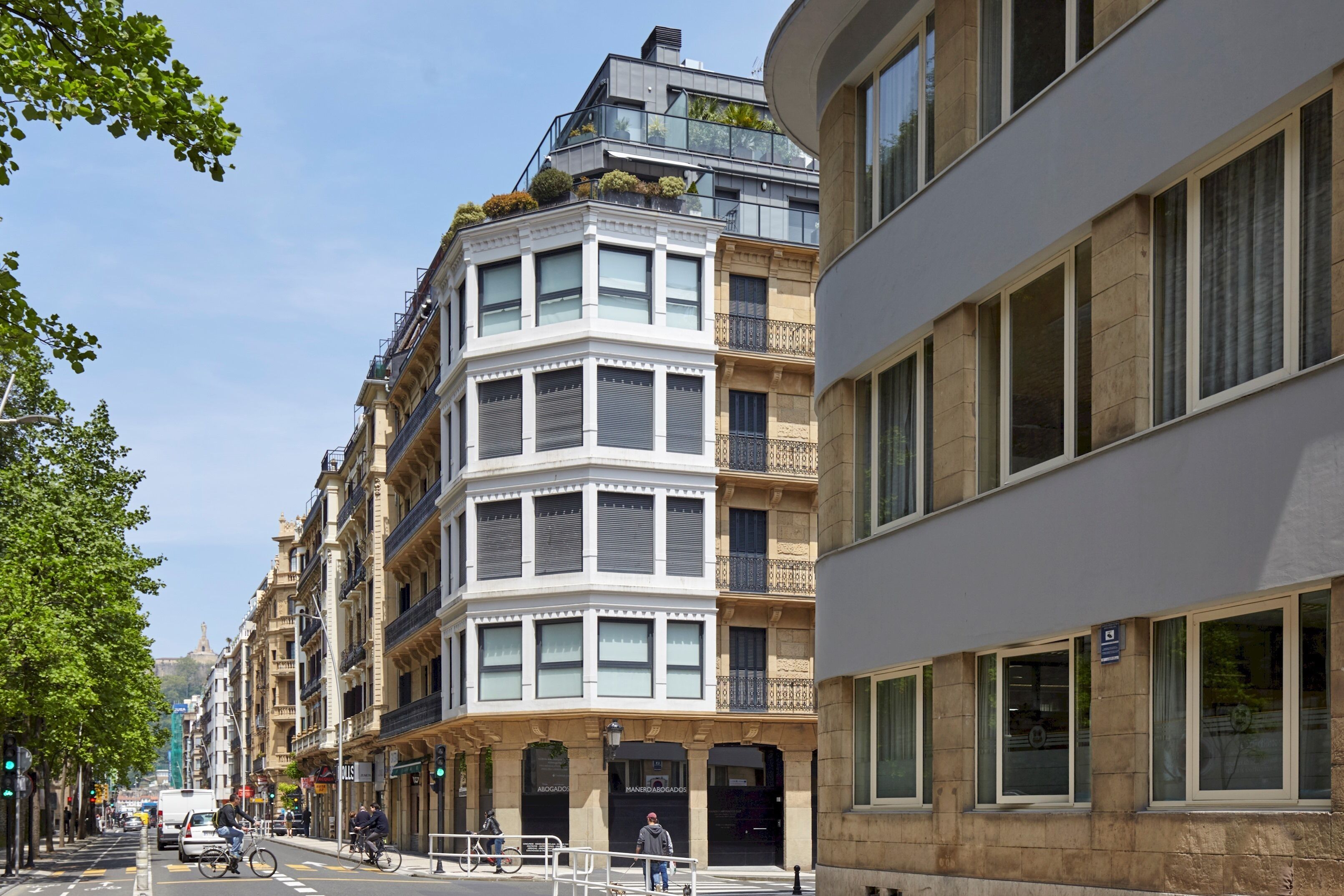 A street with multi-story buildings, including a corner building with a bay window and a flat facade.