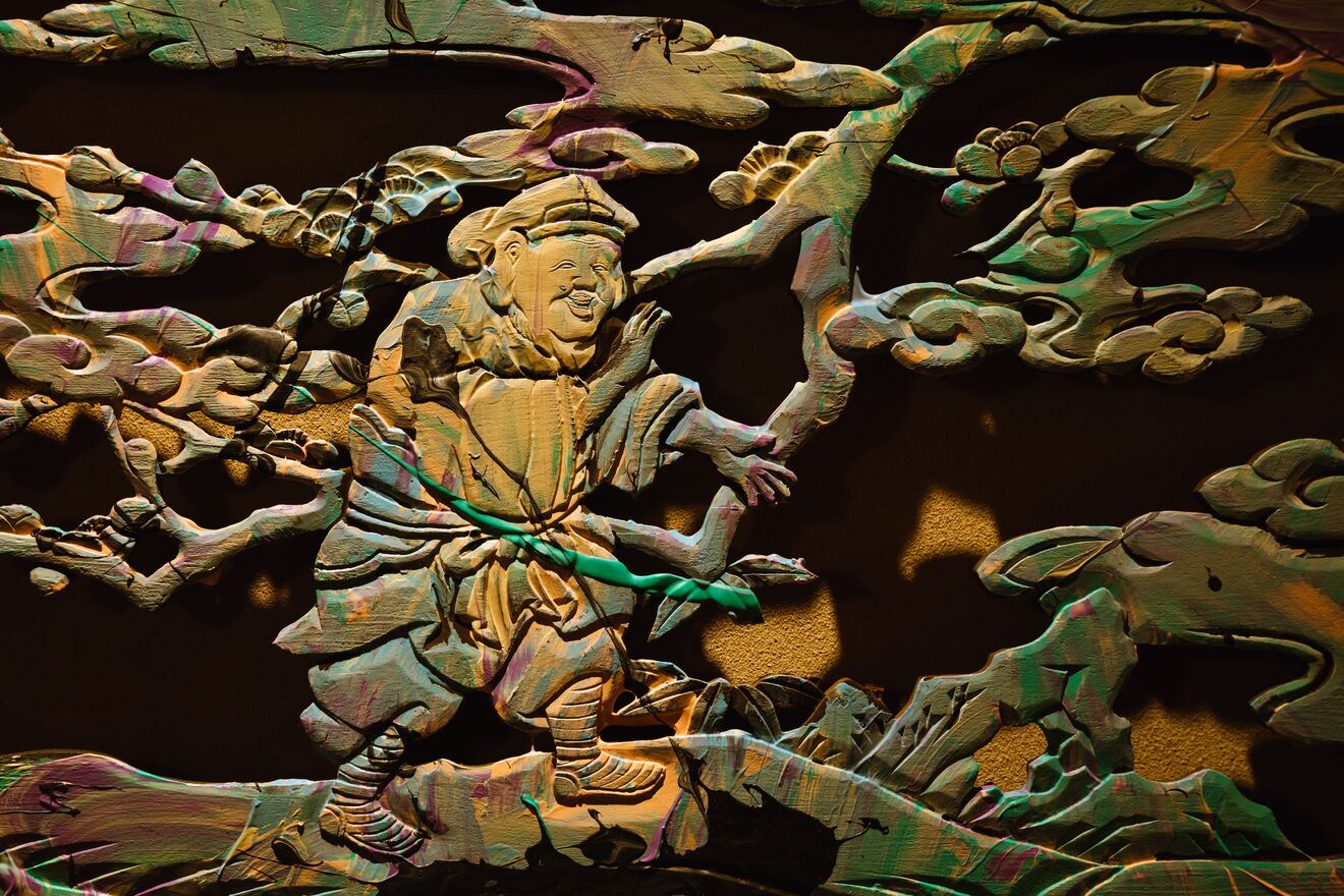 A detailed sculpture of a figure with outstretched arms, set against a dark background with intricate cloud-like patterns.
