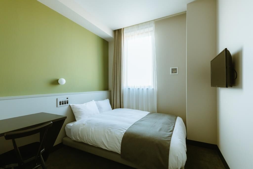 Een hotelkamer met een bed, een bureau, een stoel, een televisie en een raam met gordijnen.