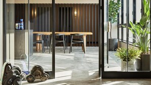 A modern office space with a glass partition, a wooden table with chairs, and potted plants. - Hotel Karae - Hostel (Karatsu)