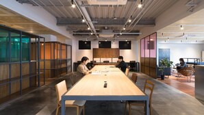 A modern office space with a long wooden table, conference room, and glass partitions. - Hotel Karae - Hostel (Karatsu)