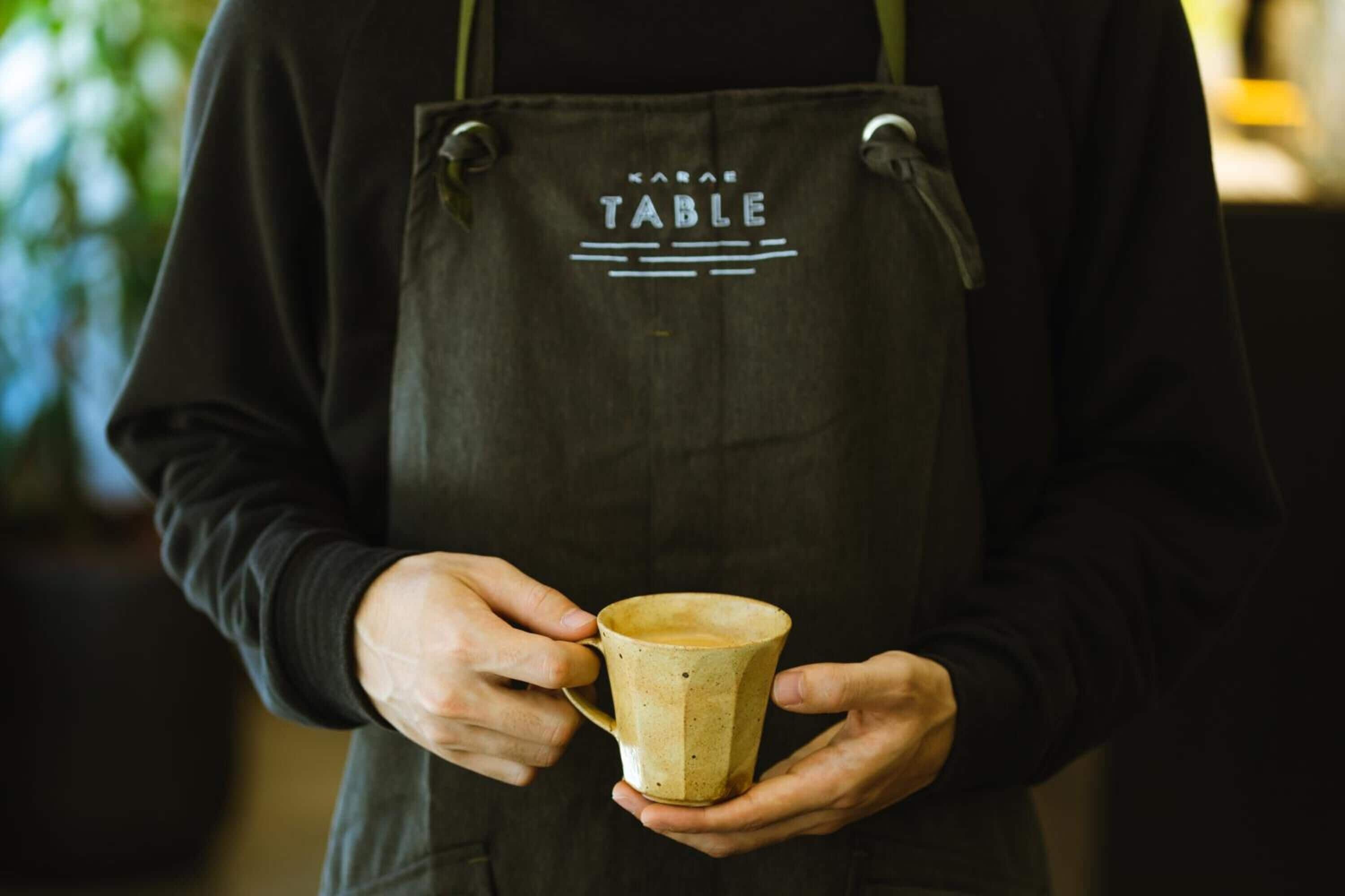 A person holding a mug with a label that reads "KARAS TABLE".