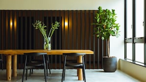A modern dining area with a wooden table, black chairs, a vase with green plants, and a large potted plant. - Hotel Karae - Hostel (Karatsu)