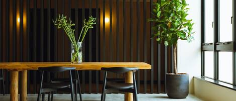 Un comedor moderno con una mesa de madera, sillas negras, un jarrón con plantas verdes y una planta en maceta grande.