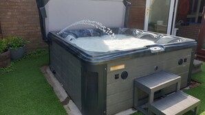 A hot tub with a wooden bench and a small step for access, surrounded by artificial grass and a brick wall. - Eastwatch Guesthouse (Berwick-upon-Tweed)