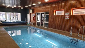 An indoor swimming pool with wooden paneling, clear glass doors, and a safety sign. - Eastwatch Guesthouse (Berwick-upon-Tweed)