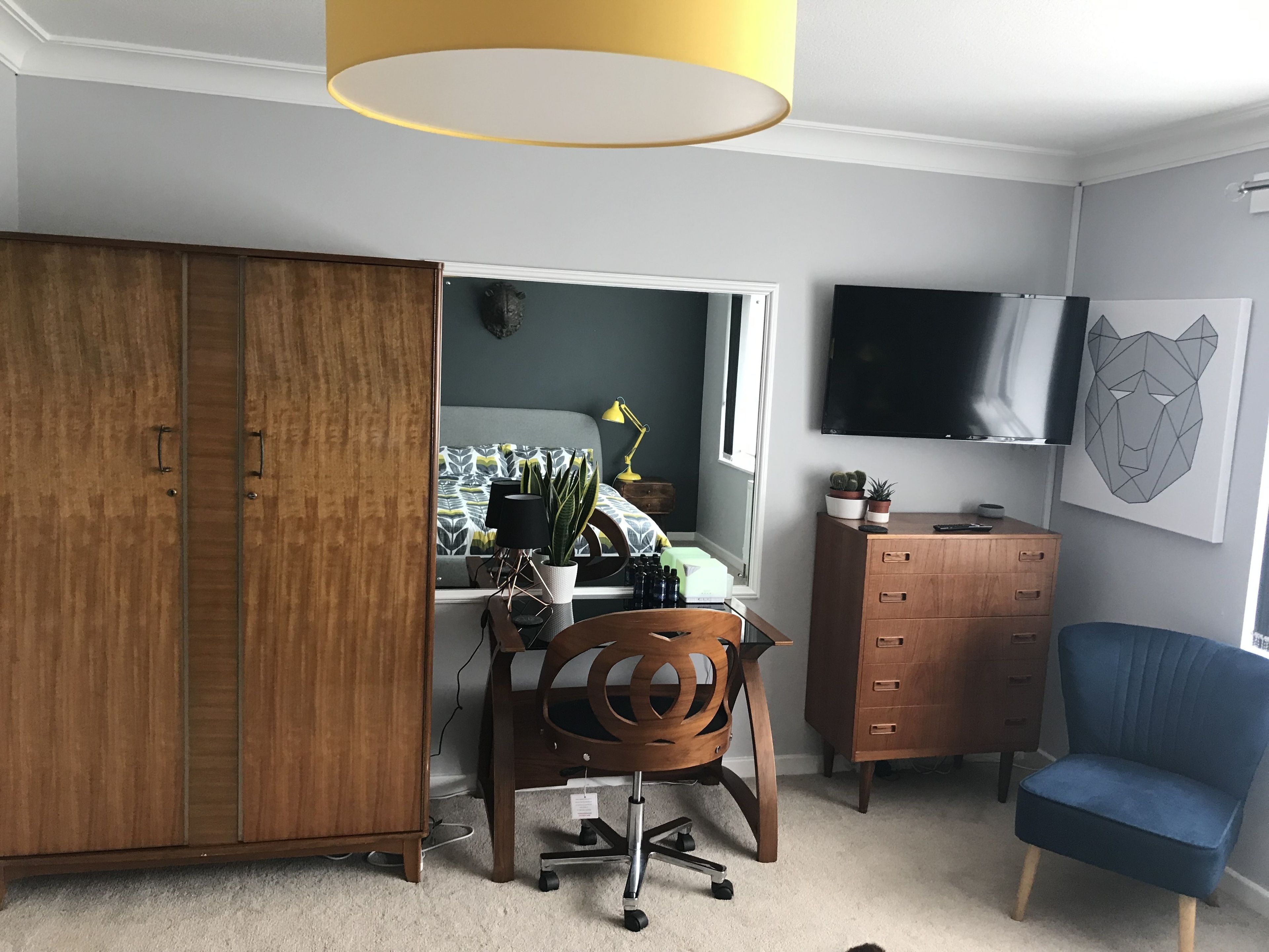 Ein Schlafzimmer mit Kleiderschrank, Schreibtisch mit Stuhl, Kommode, Fernseher und Wandbild.