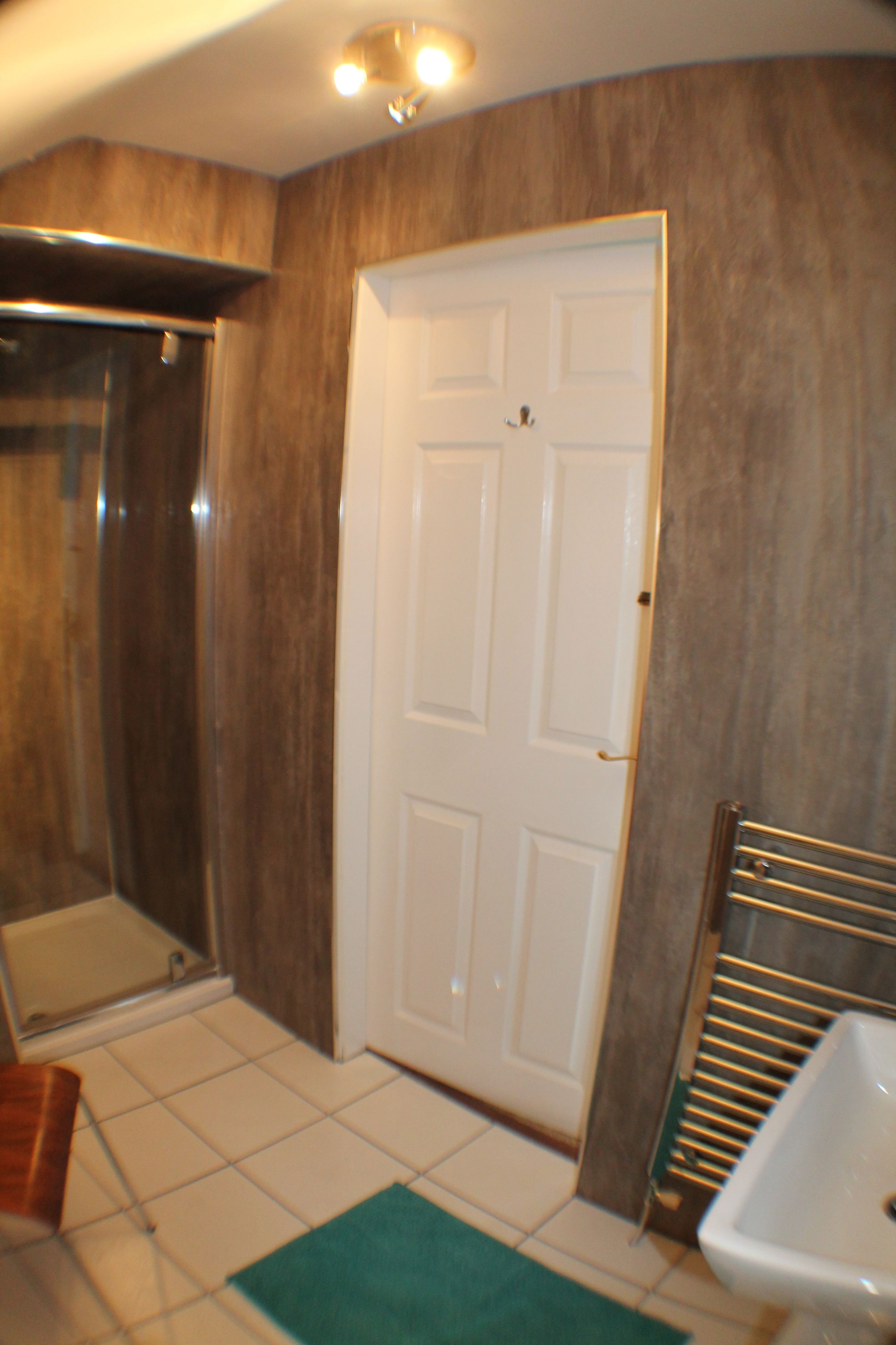 A bathroom with a white door, a shower, and a sink.