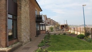 A residential building with a brick facade, large windows, and a small garden area with a lawn and plants. - Eastwatch Guesthouse (Berwick-upon-Tweed)