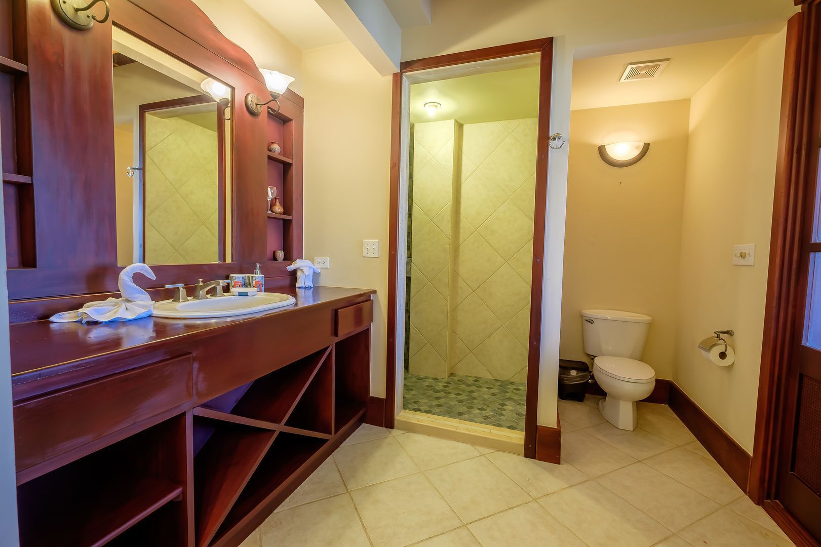 Een badkamer met een houten wastafelmeubel, een spiegel, een douche met glazen deur en een toilet.