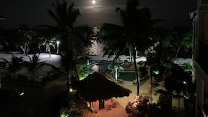 A nighttime view of a resort with a pool, palm trees, and a thatched-roof hut. - 506 - 3rd Floor Ocean View Suite (San Pedro)