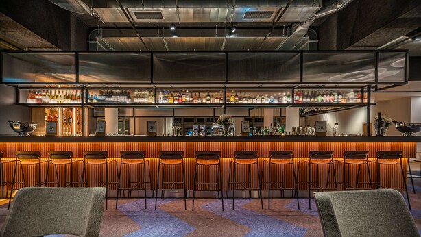 A bar area with multiple stools and a bar counter displaying various bottles. - Park Inn By Radisson Wismar (Wismar)