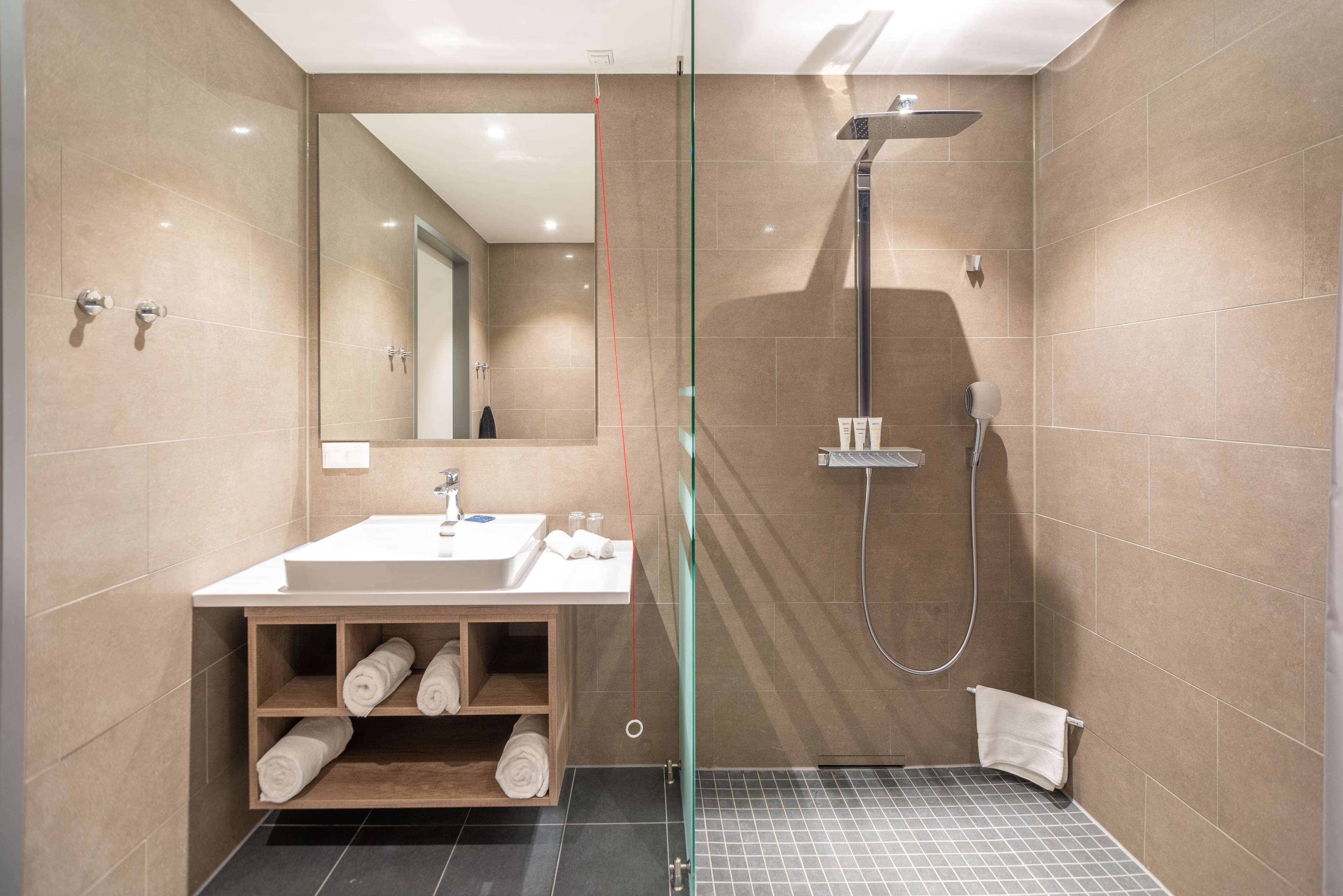Ein modernes Badezimmer mit einer Duschkabine aus Glas, einem Waschbecken mit Spiegel und einem Handtuchhalter.