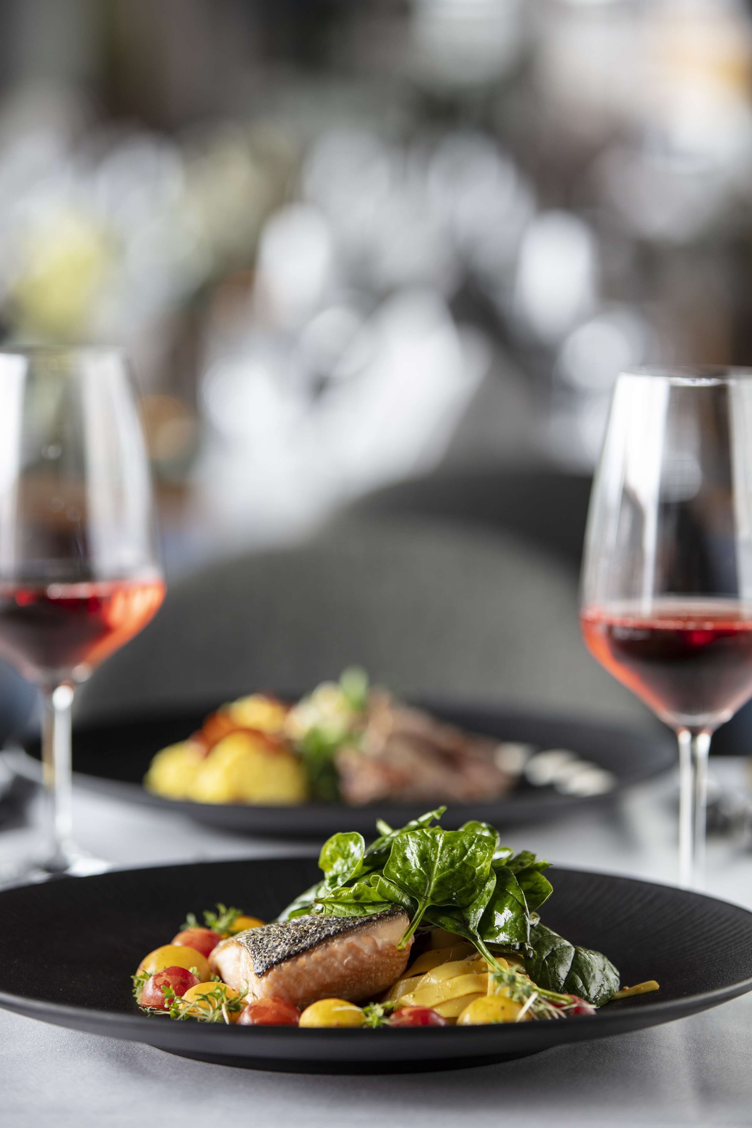 Una mesa de comedor con platos de comida y copas de vino tinto.