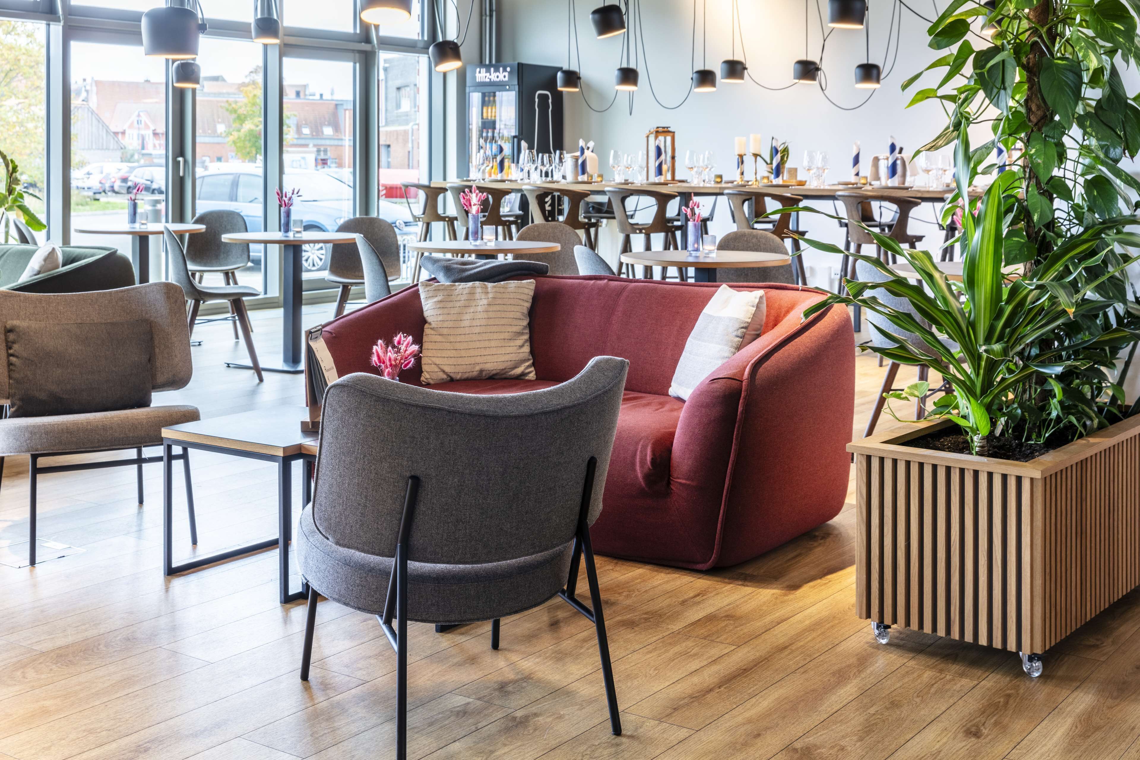 A modern cafe with wooden flooring, comfortable seating, and large windows offering a view of the street.