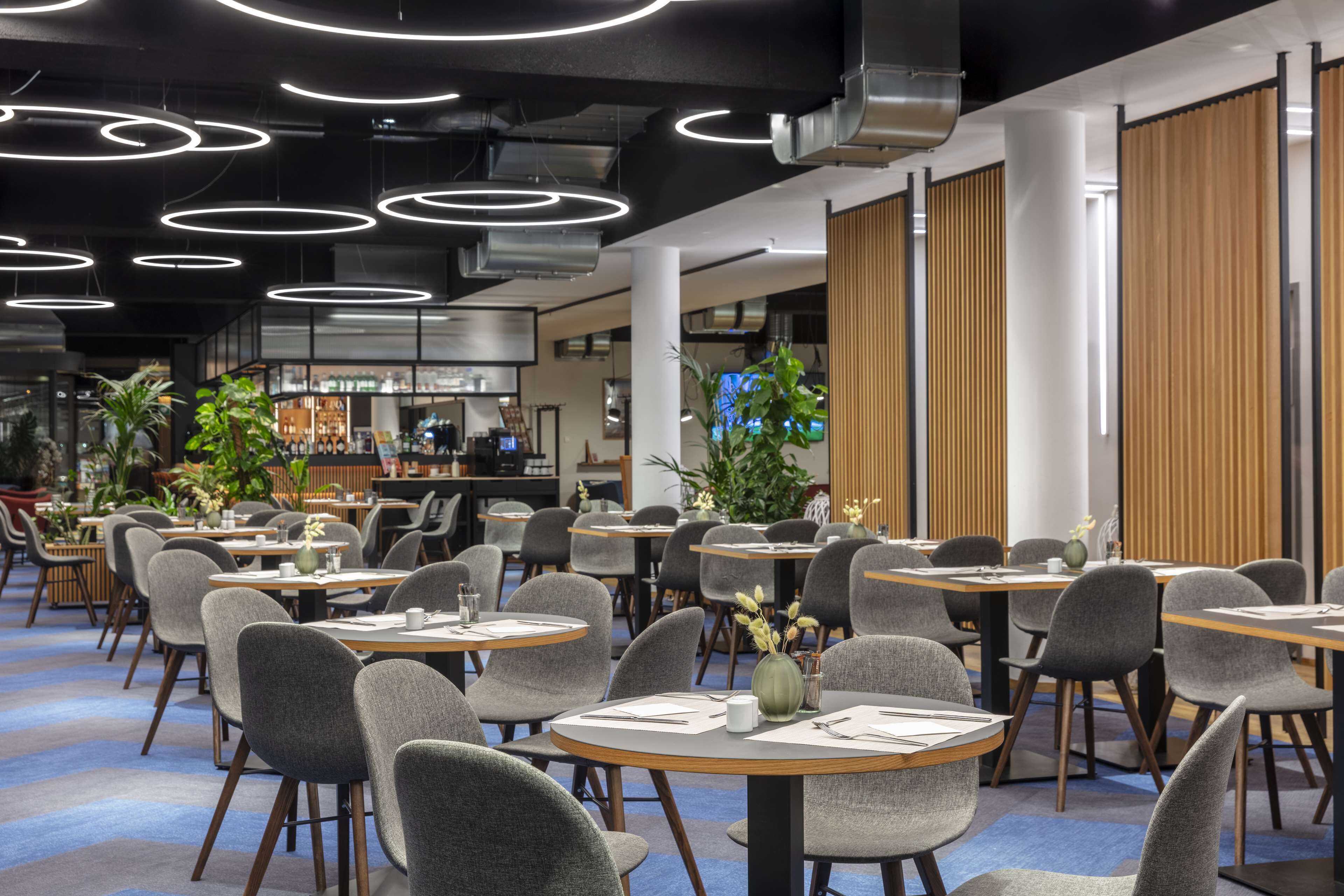 A modern dining area with round tables, grey chairs, and overhead circular lighting.