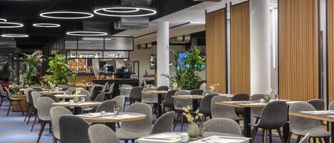 A modern dining area with round tables, grey chairs, and overhead circular lighting.
