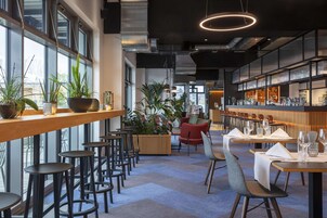 A modern restaurant with high ceilings, exposed ductwork, and a mix of bar and dining areas.