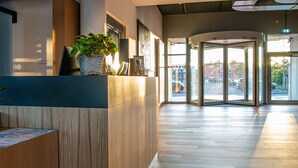 A modern reception area with a wooden reception desk, a potted plant, and a glass door leading outside. - Park Inn By Radisson Wismar (Wismar)