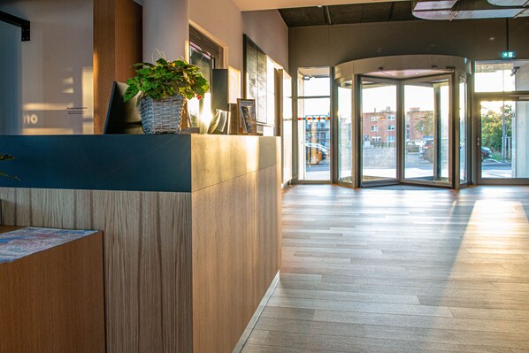A modern reception area with a wooden reception desk, a potted plant, and a glass door leading outside.