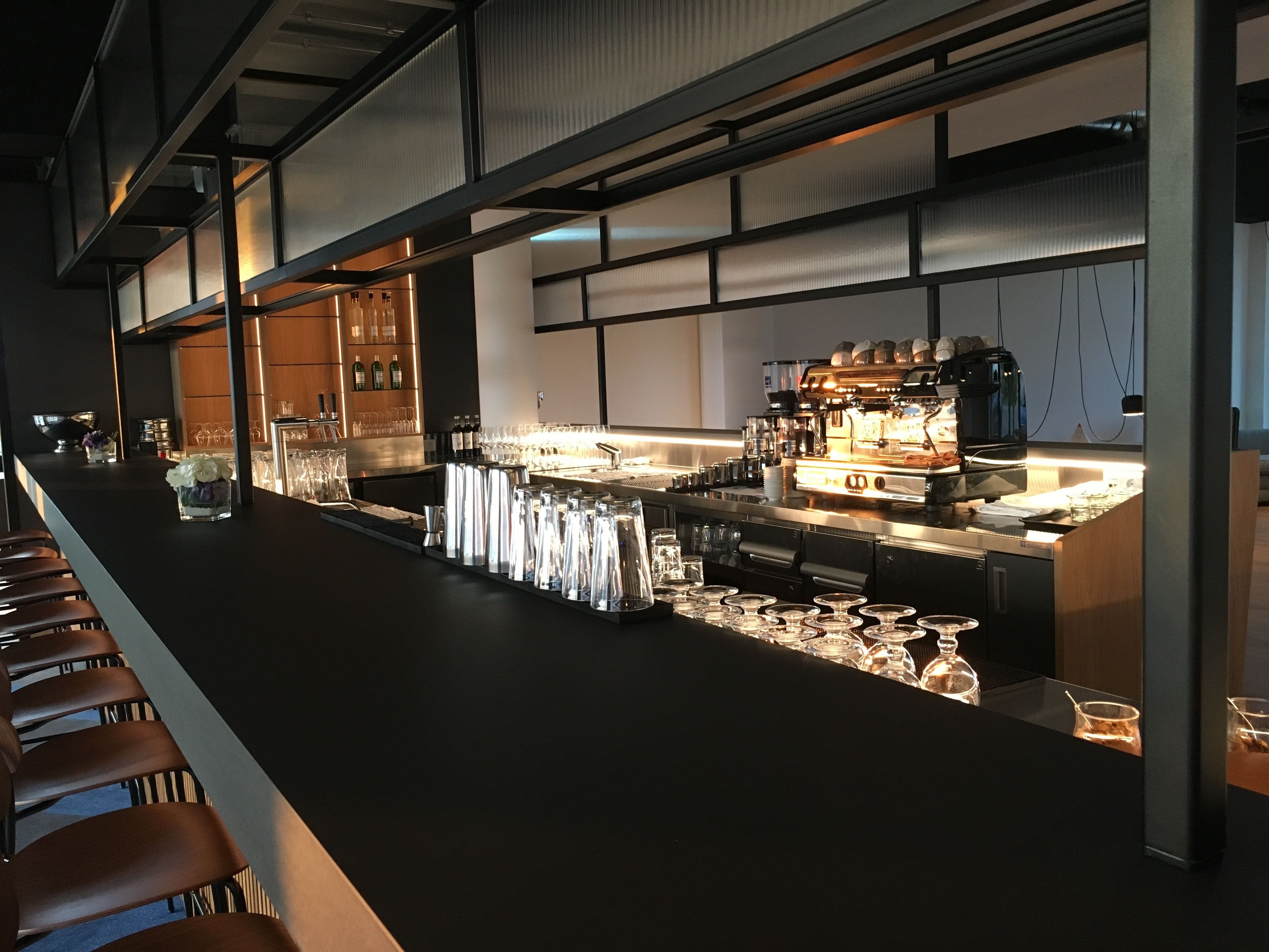 A modern bar area with a long counter, bar stools, and a coffee machine.