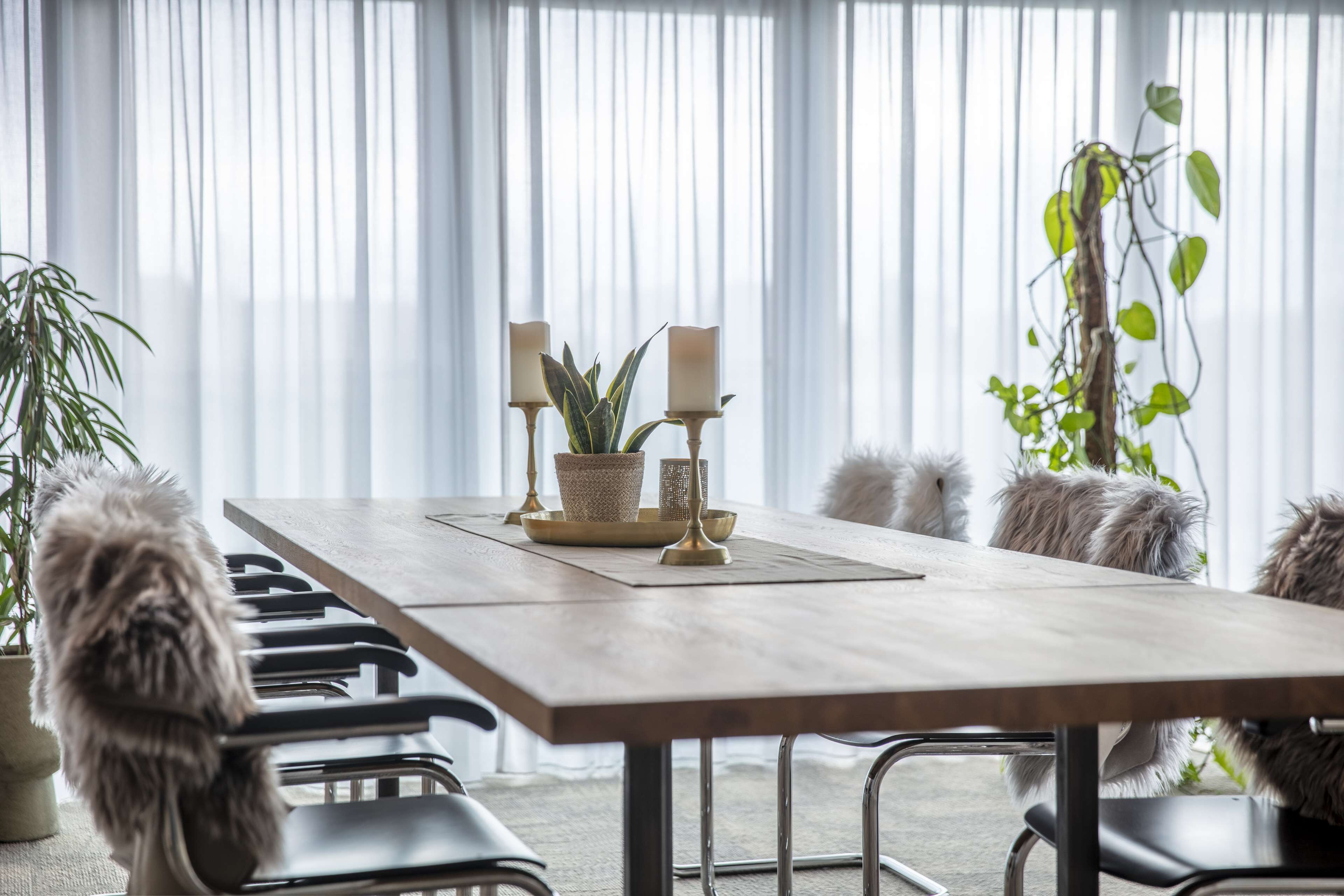 A dining area with a wooden table, chairs, candles, and potted plants.