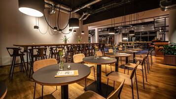 Un restaurant moderne avec des tables rondes et des chaises en bois, agrémenté de luminaires suspendus et de plantes en pot.