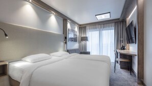 A hotel room with a large bed, a desk, a chair, a TV, and a window with curtains. - Park Inn By Radisson Wismar (Wismar)