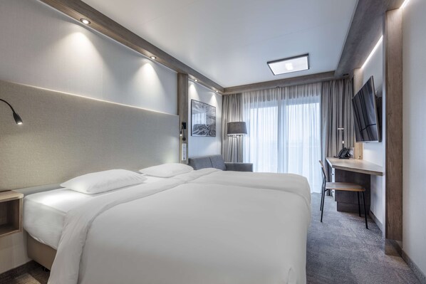 A hotel room with a large bed, a desk, a chair, a TV, and a window with curtains. - Park Inn By Radisson Wismar (Wismar)
