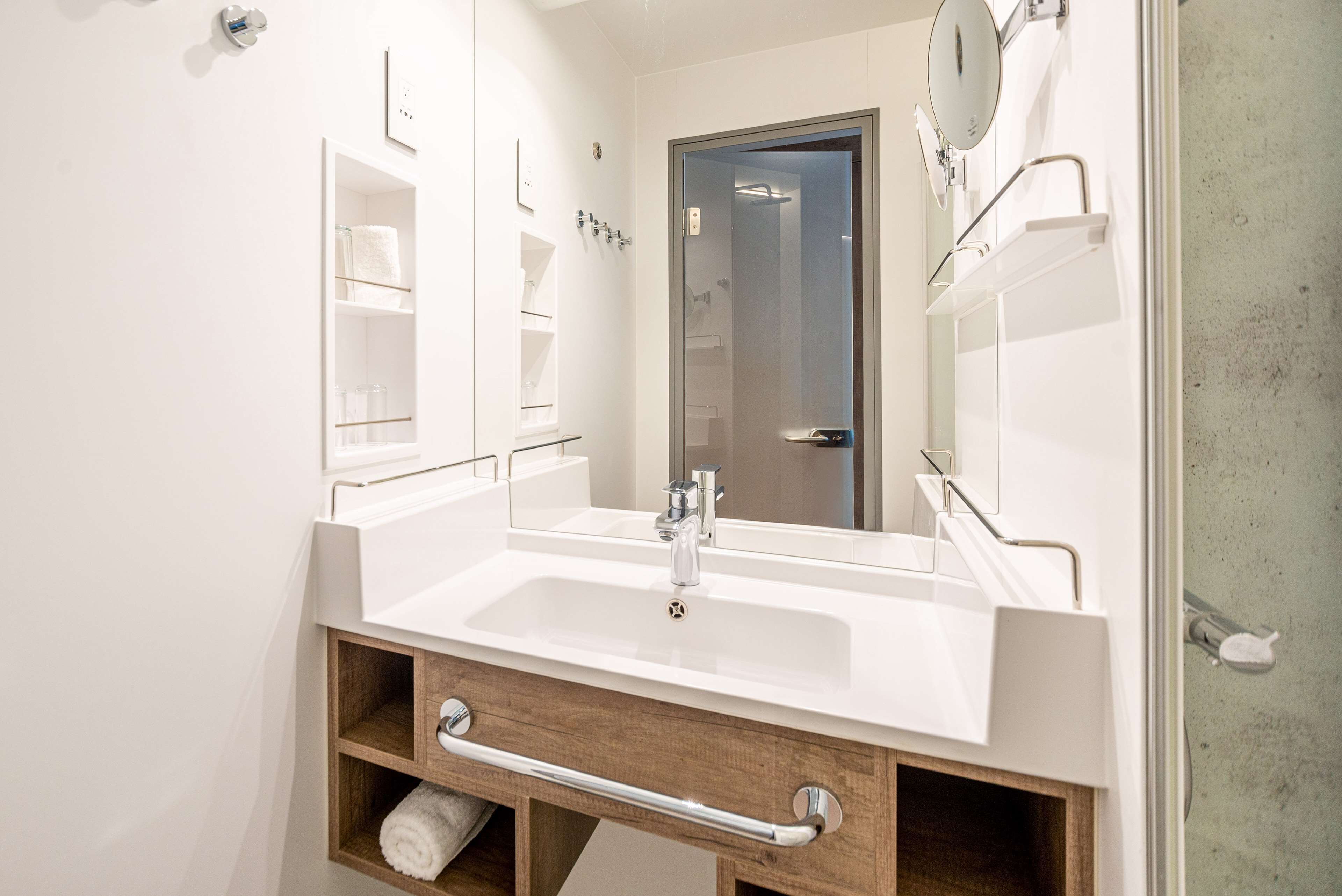 A modern bathroom with a white sink, a mirror, and a wooden vanity with a towel rack.