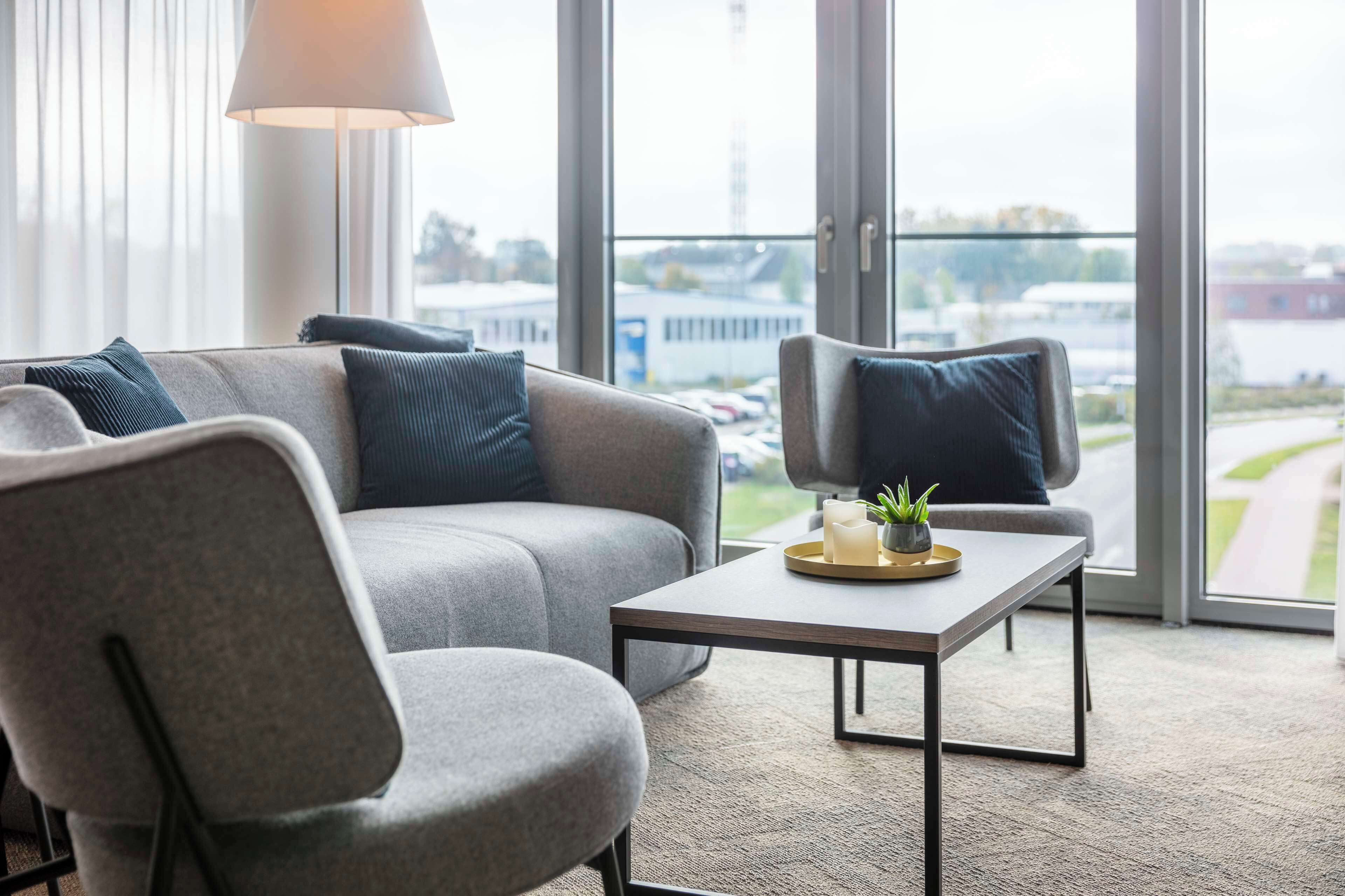 A modern living room with a grey sofa, two armchairs, a coffee table, and a lamp.