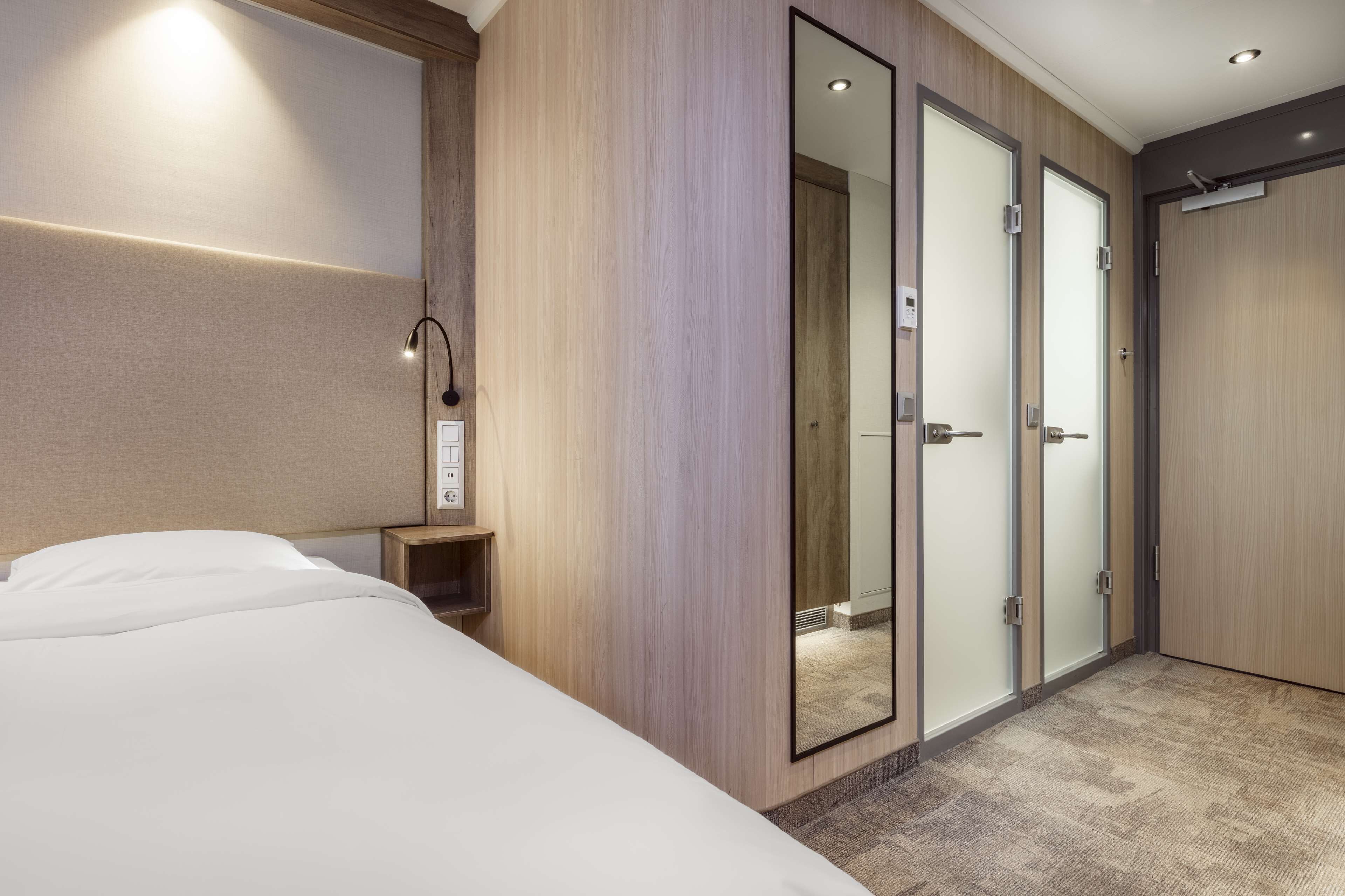 Una habitación de hotel con cama, mesita de noche, espejo y armario con puertas correderas.