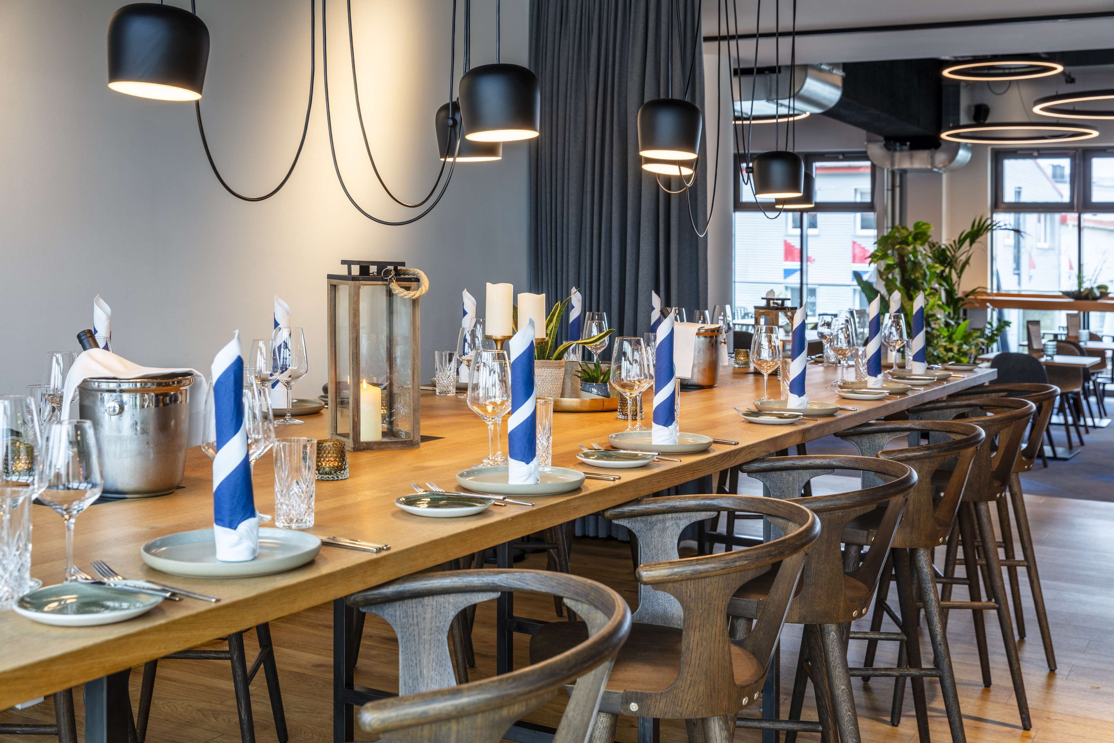 Una larga mesa de comedor dispuesta con platos, vasos y servilletas, rodeada de sillas de madera.