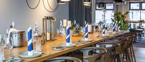 Una larga mesa de comedor dispuesta con platos, vasos y servilletas, rodeada de sillas de madera.