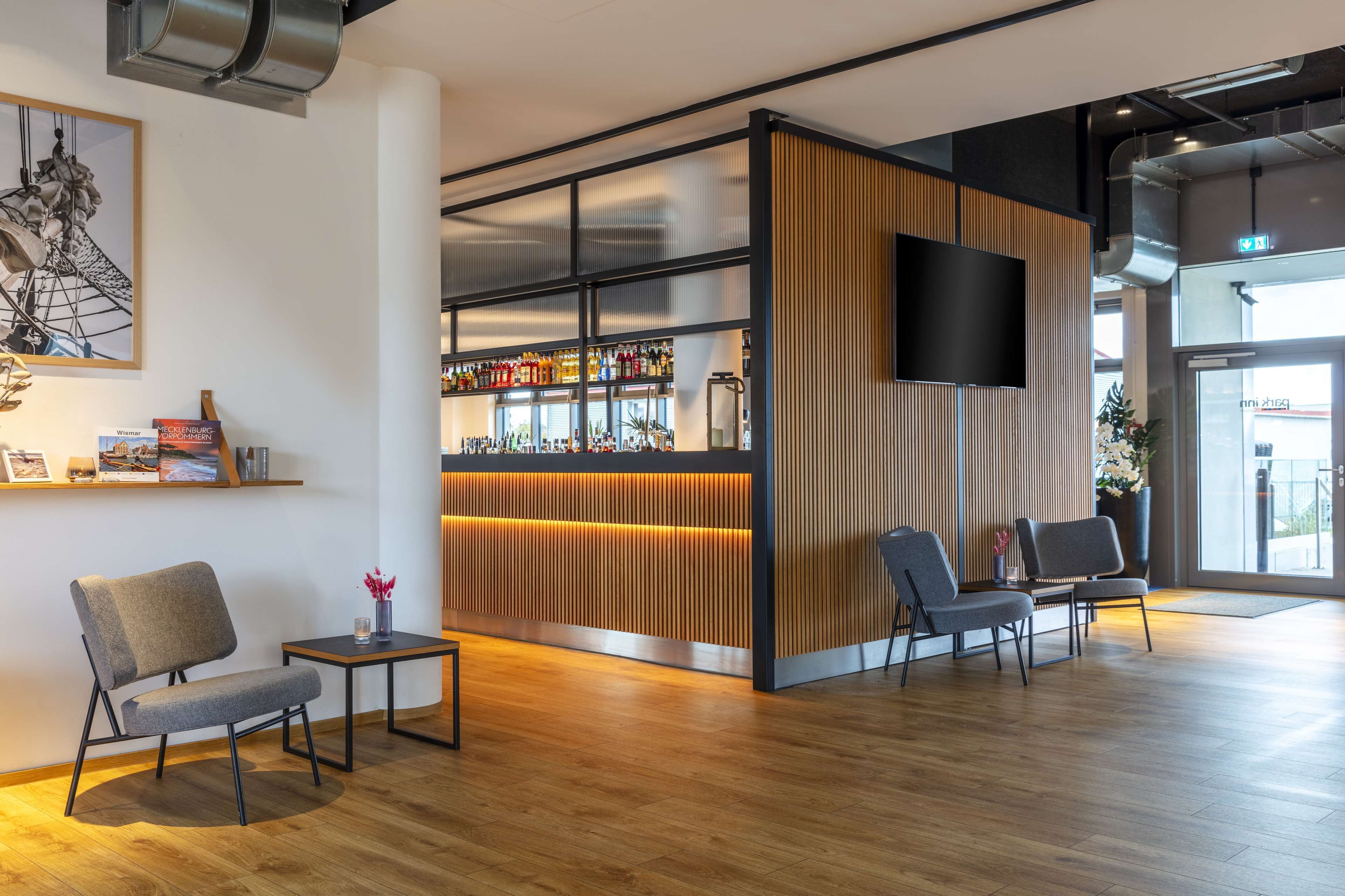 Un área de recepción moderna con un mostrador de madera, un televisor montado y una zona de bar con estantes llenos de botellas.