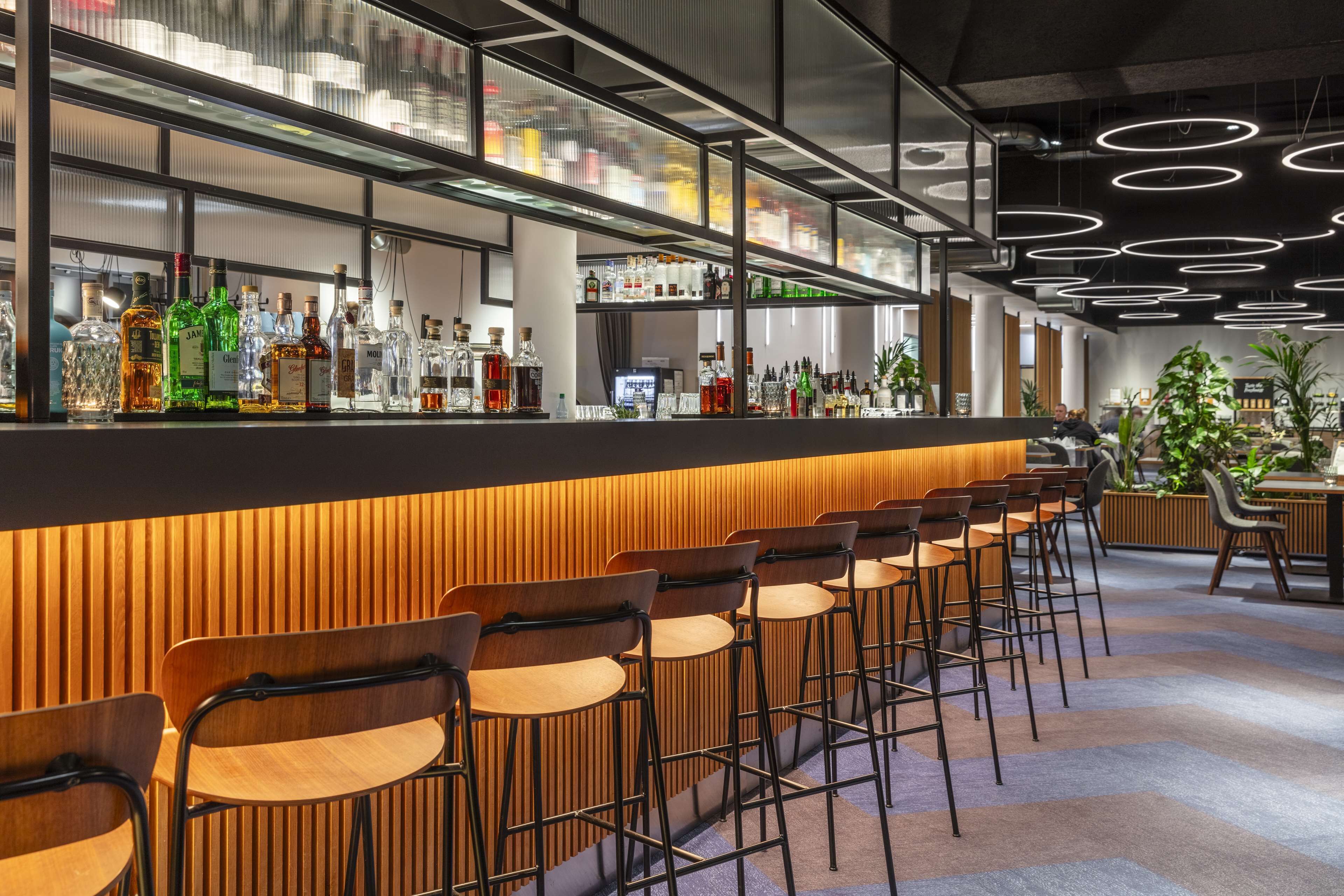 A bar area with a long counter, multiple stools, and a variety of bottles.
