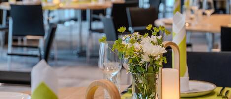 Een eettafel gedekt met borden, bestek, een kaars en een vaas met bloemen.