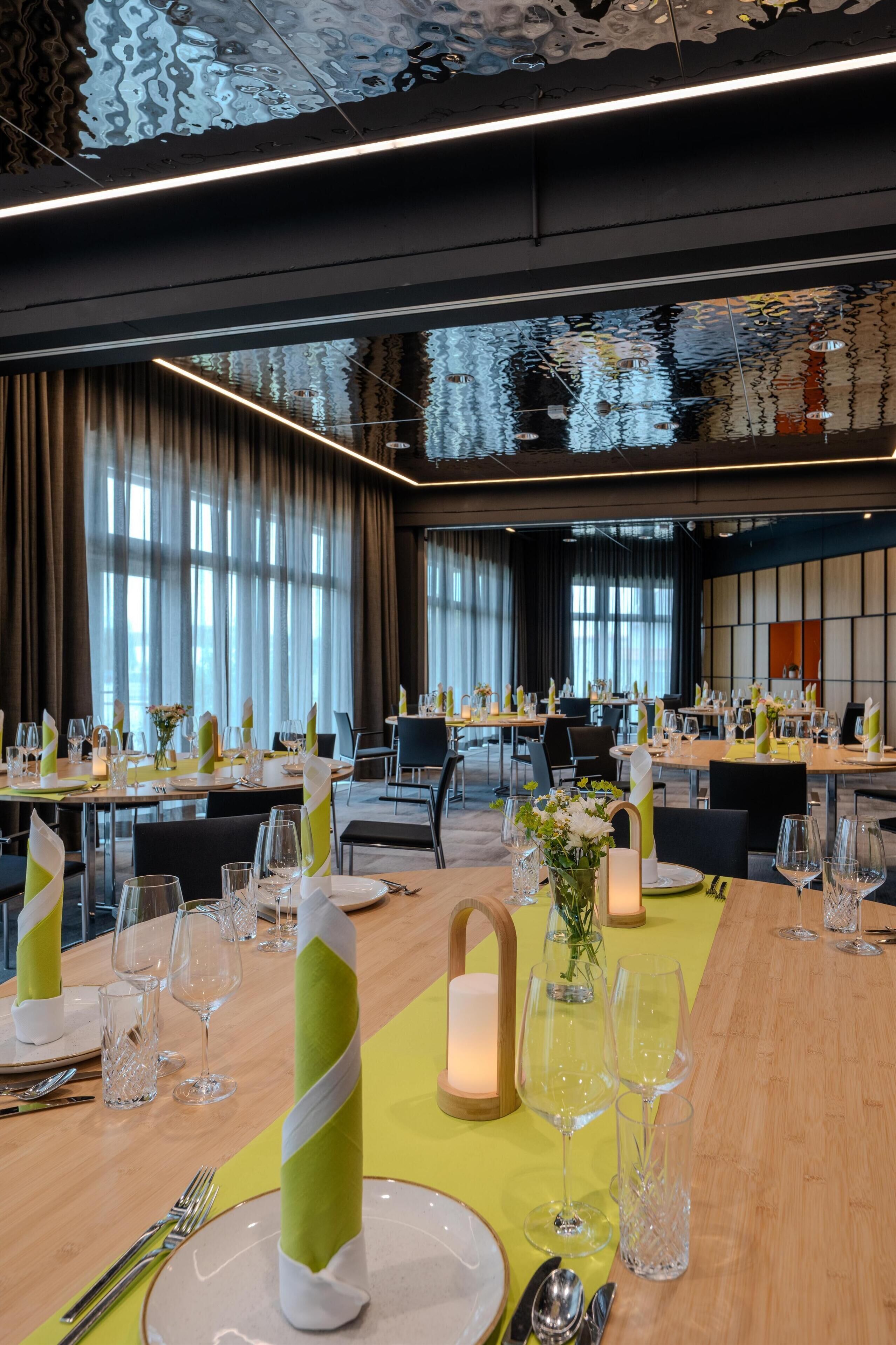 A well-lit banquet hall with tables set for a formal event, featuring reflective ceiling and large windows.