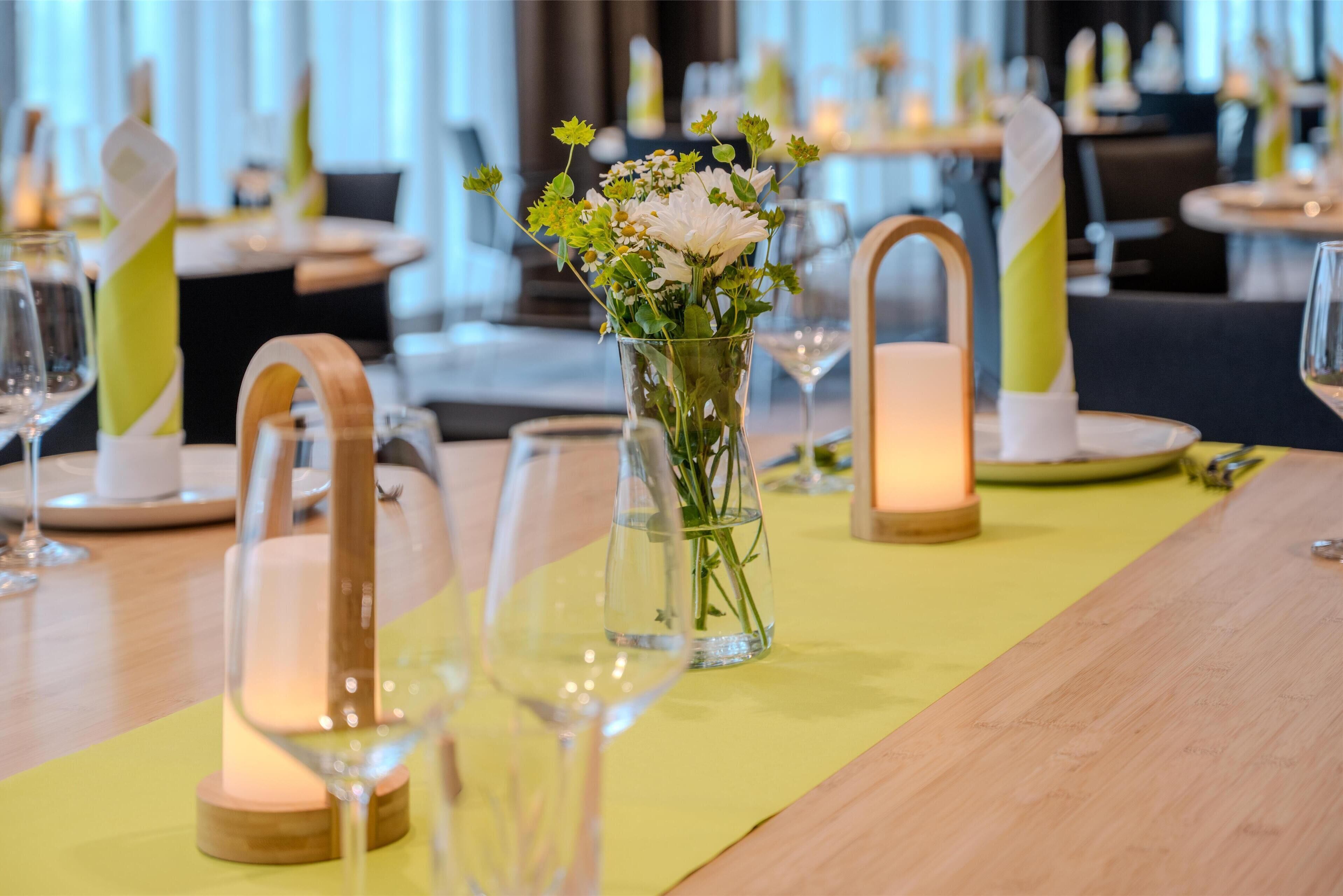 Una mesa de comedor dispuesta con un florero de cristal transparente, velas y copas de vino.