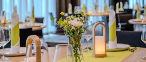 Una mesa de comedor dispuesta con un florero de cristal transparente, velas y copas de vino.