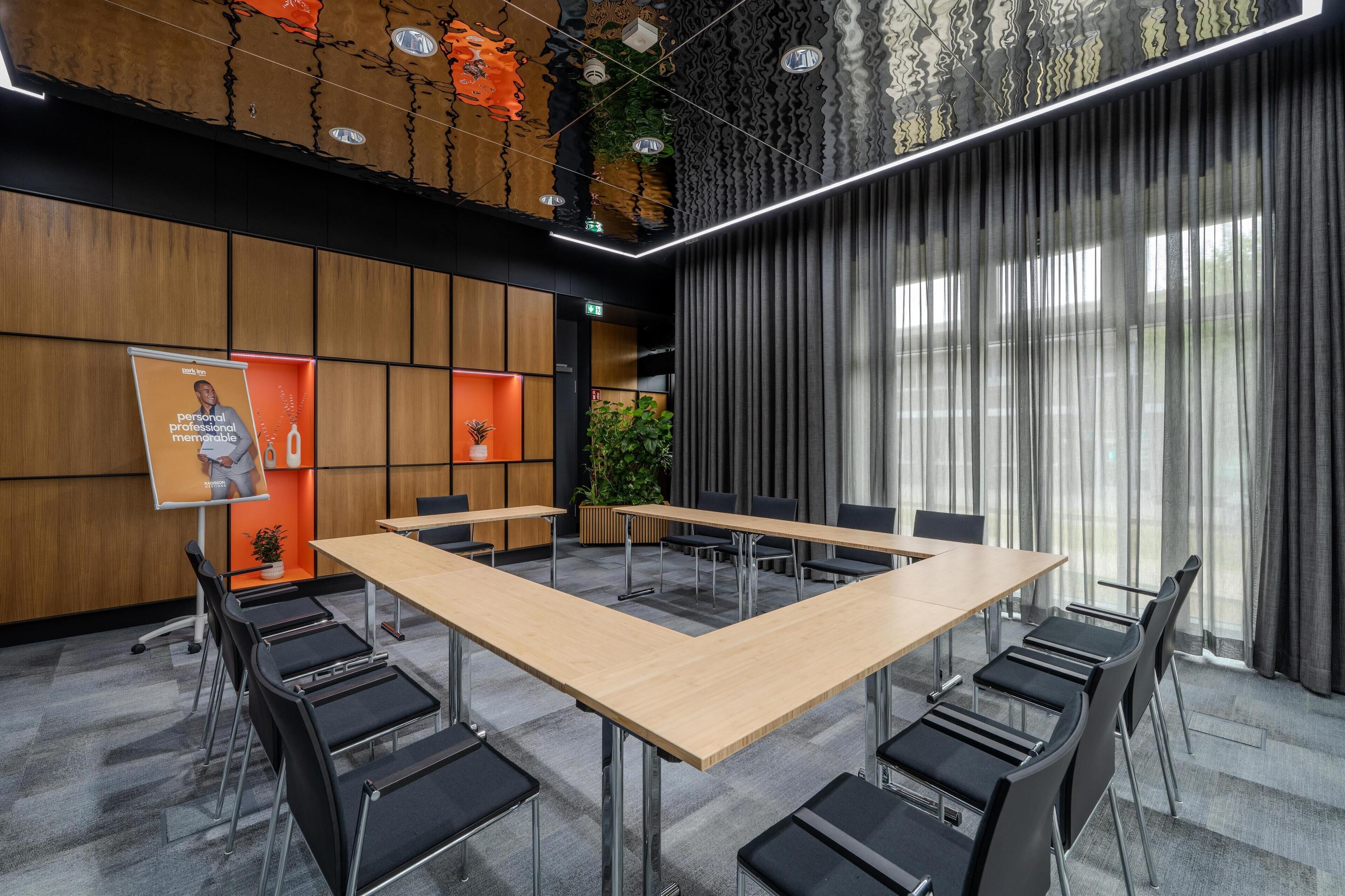 Une salle de conférence moderne, dotée d’une grande table, de chaises noires et d’un mur recouvert de panneaux en bois.