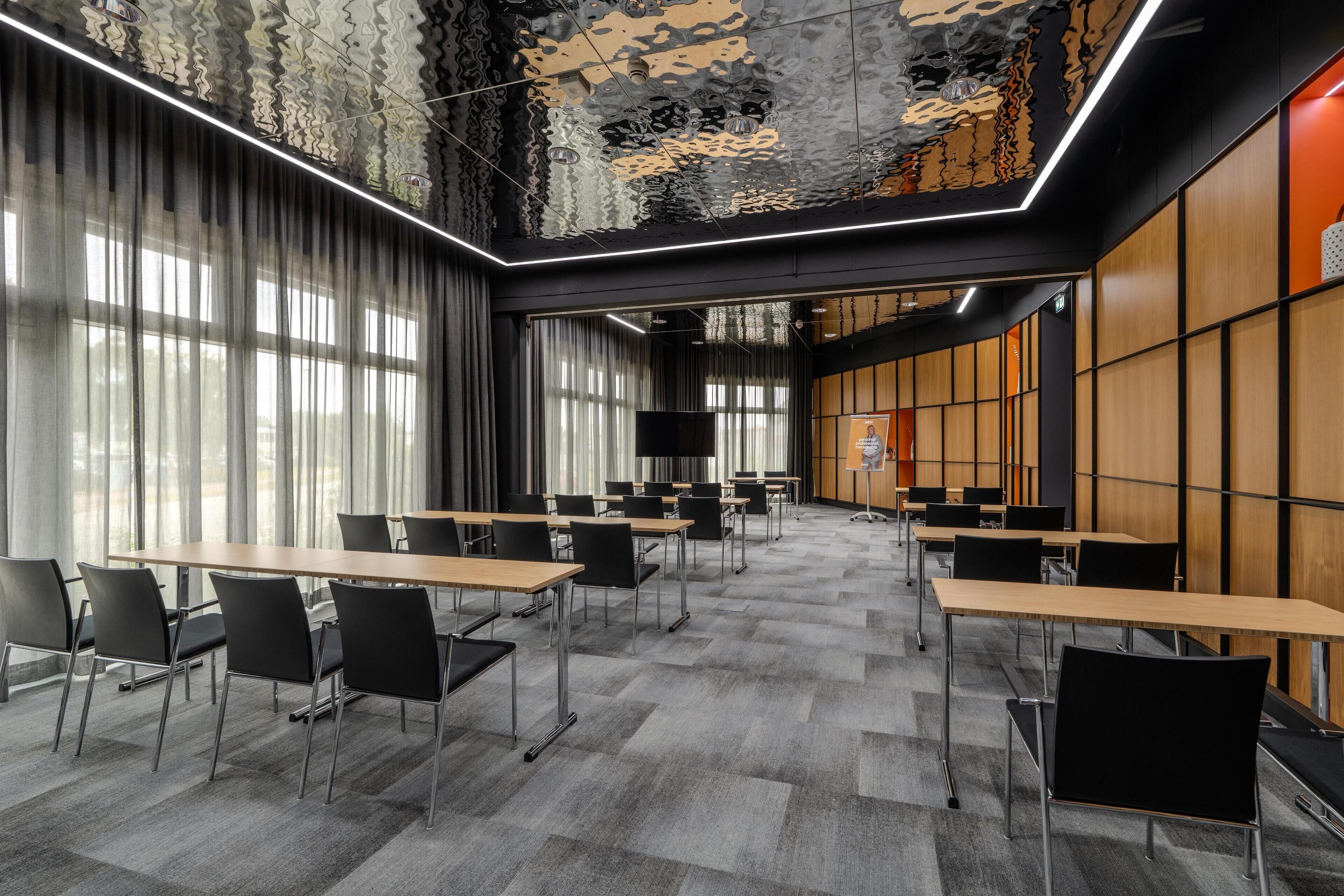 Un salón de conferencias con mesas, sillas, ventanas amplias y un techo con diseño.